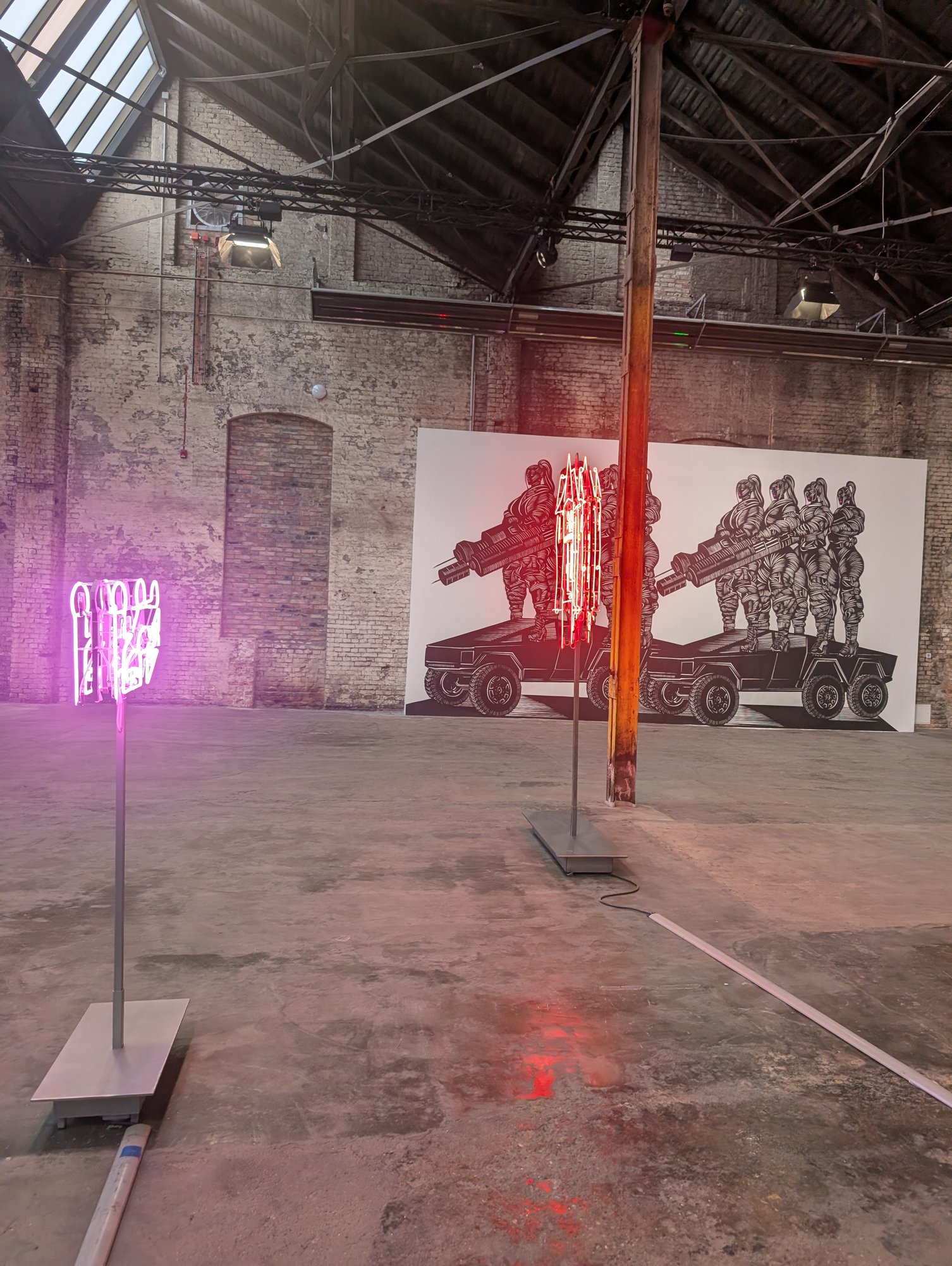 Schwarzweiße Zeichnung mit Figuren auf gepanzerten Fahrzeugen, davor zwei Neonobjekte, HALLEN 07 in den Wilhelm Hallen