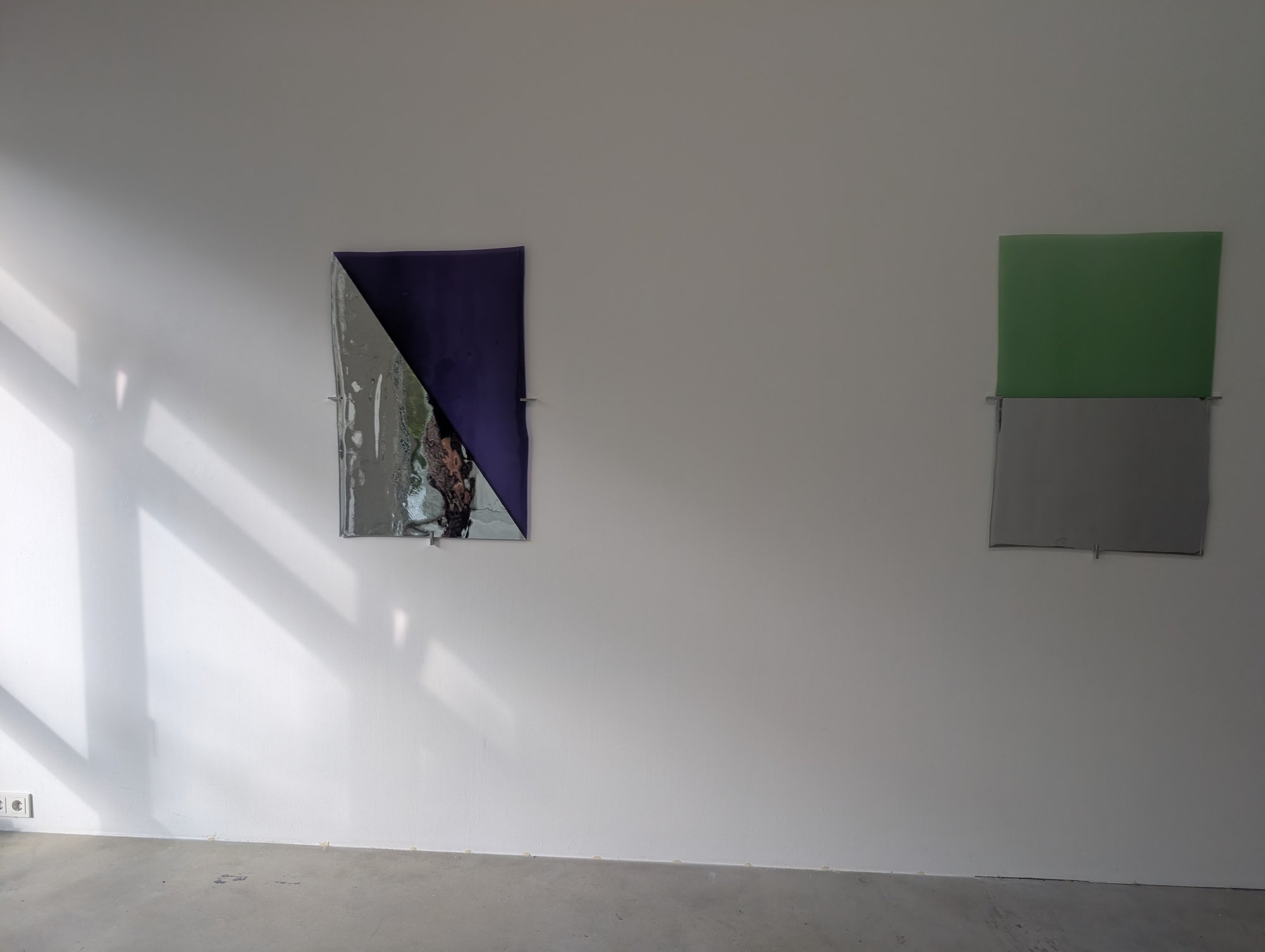 Gebogene Platten, halb farbig, halb spiegelnd, auf Metallstiften, daneben der Schatten eines Fensterkreuzes, erste Station des Rundgangs